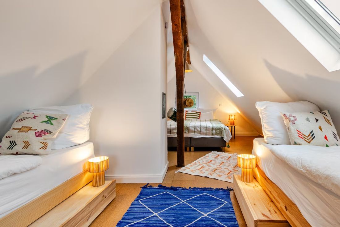 Dachzimmer mit Holzbalken, Betten und blauem Teppich