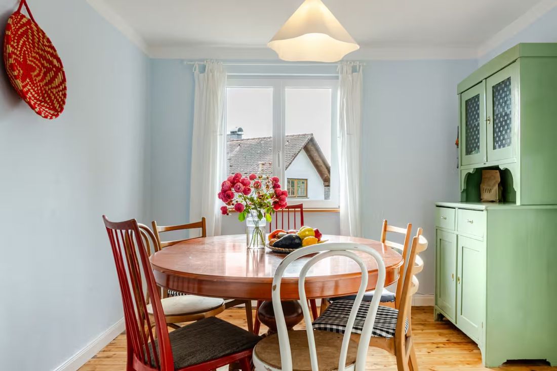 Esstisch mit Rosen vor hellblauen Wänden und grünem Buffetschrank