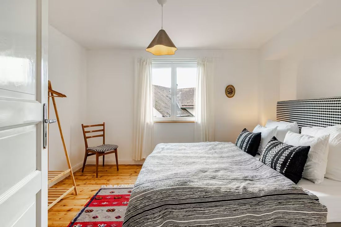 Schlafzimmer mit grauer Bettwäsche und buntem Teppich