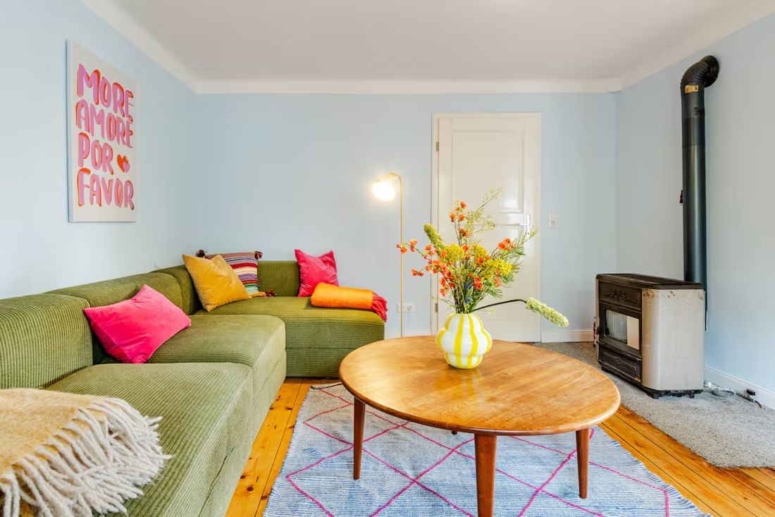 Wohnzimmer mit grünem Sofa, buntem Teppich und Ofen