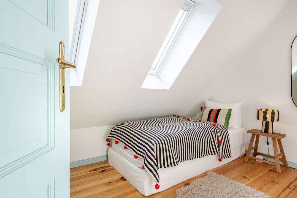 Dachzimmer mit Einzelbett, gestreifter Decke und hellblauer Tür