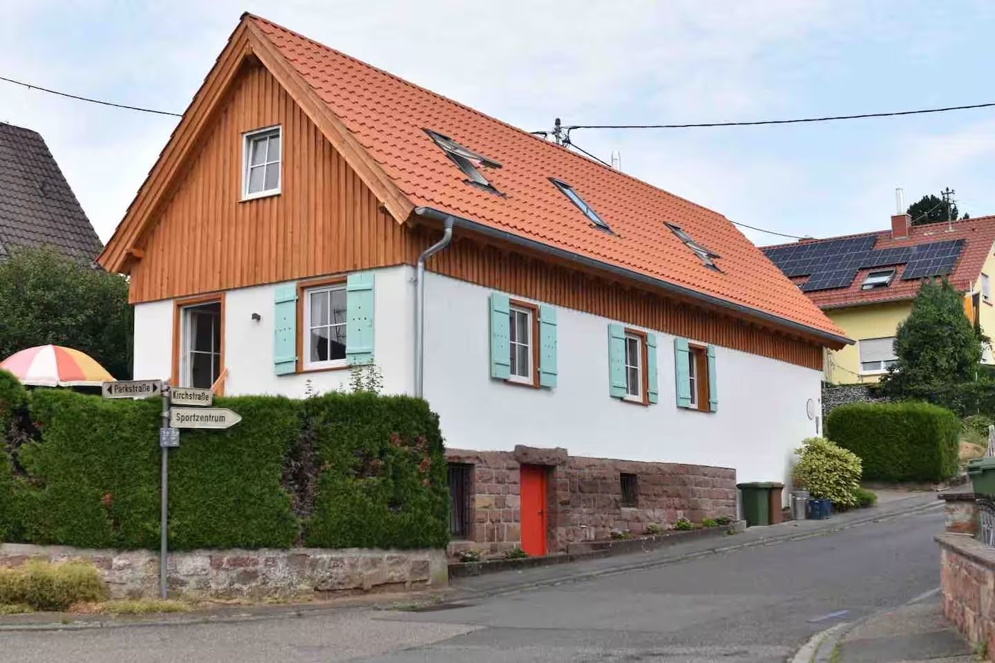 Außenansicht des Feni mit Holzgiebel, roter Tür und mintfarbenen Fensterläden