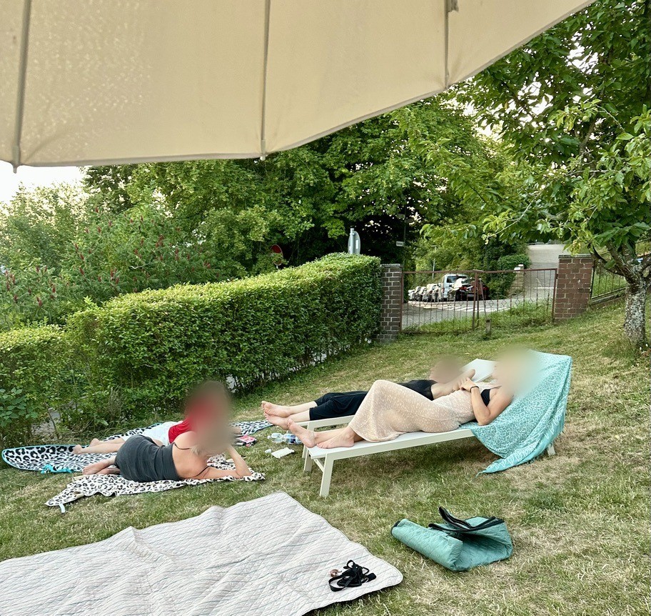 Freundinnen entspannen auf Decken und einer Liege im Garten unter dem Sonnenschirm