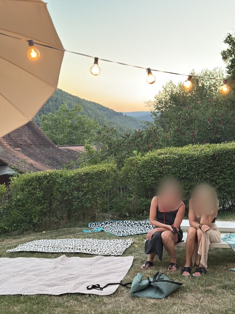 Zwei Frauen sitzen abends im Garten unter einer Lichterkette, im Hintergrund das Neckartal