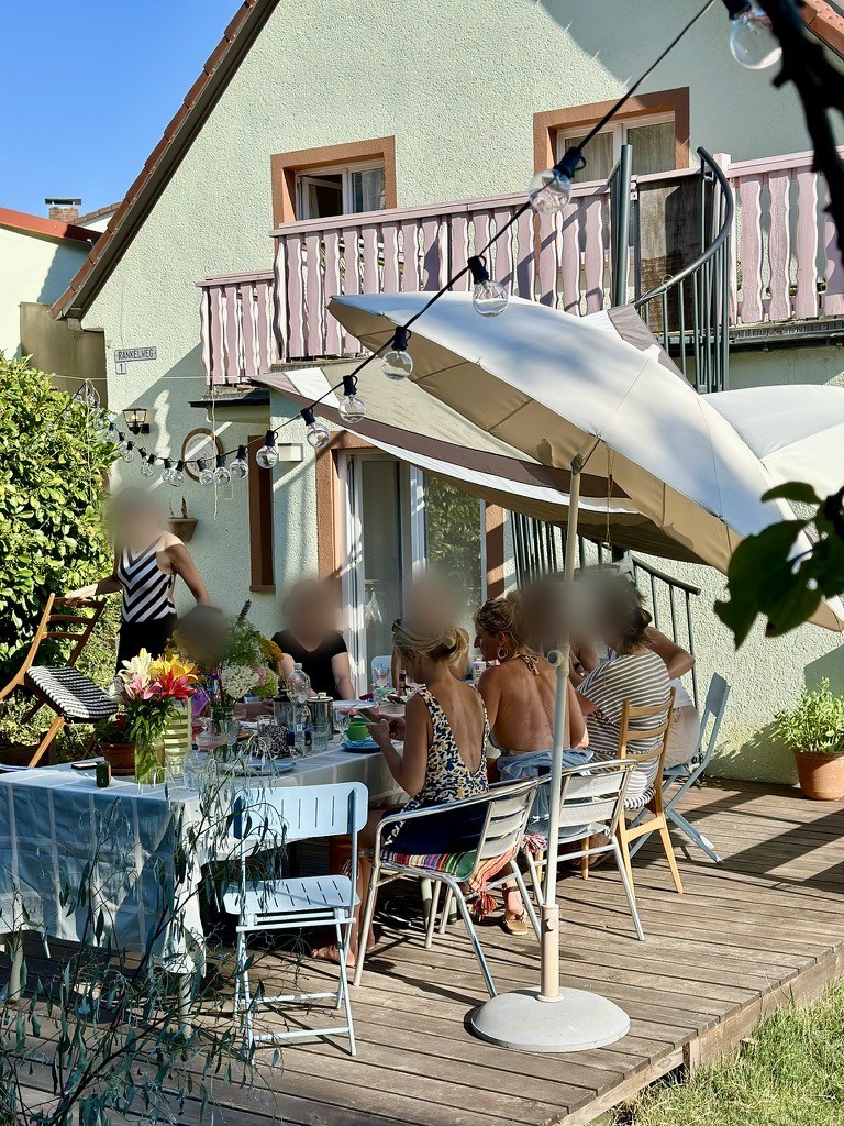 Gedeckter Tisch auf der Terrasse mit Blumen, Sonnenschirm und Lichterkette