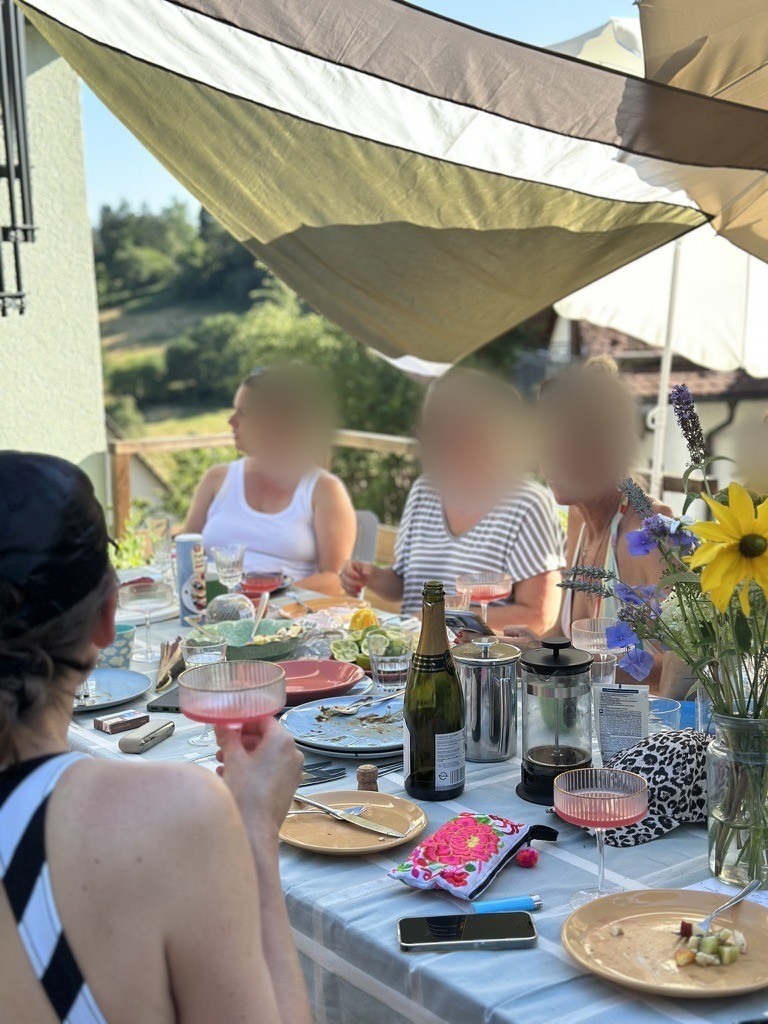 Tisch auf der Terrasse mit rosa Gläsern, Sekt und Wildblumen im Sonnenlicht