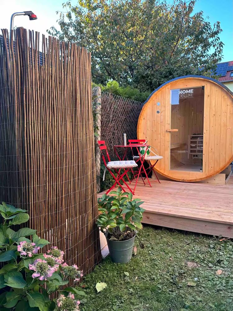 Fasssauna im Garten mit roten Stühlen