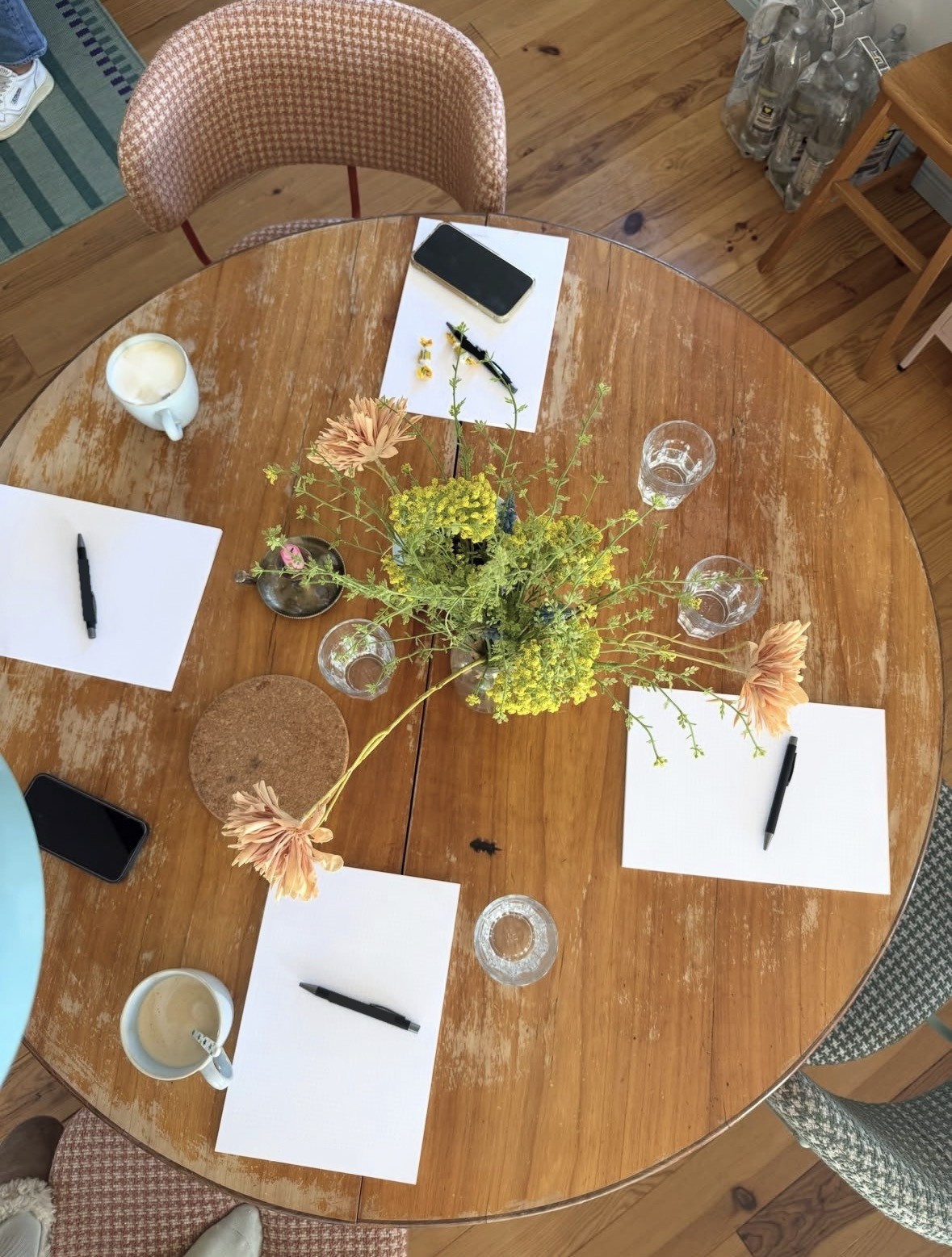 Runder Holztisch von oben mit Wildblumen, Notizblöcken, Stiften und Kaffee